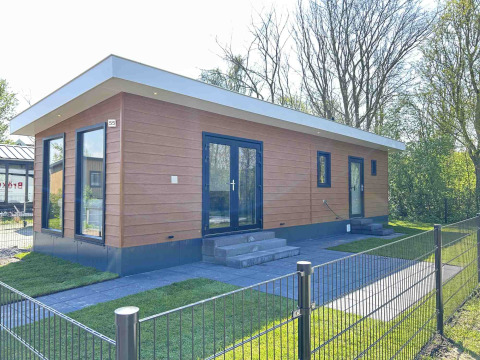 Moderna cabaña en Parkzicht, Vakantiepark de Zeeuwse Parel, Países Bajos, rodeada de césped y árboles.