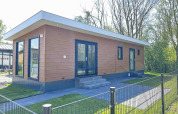 Modern lodge at Parkzicht in Vakantiepark de Zeeuwse Parel, Netherlands, with lawn, trees and fenced yard.