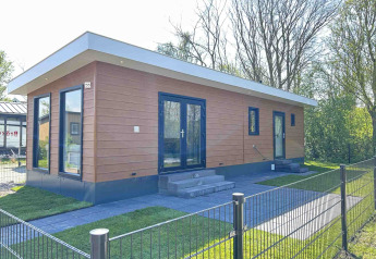 Moderne lodge ved Parkzicht i Vakantiepark de Zeeuwse Parel, Holland, omgivet af græsplæne og træer.