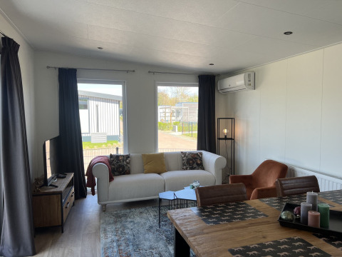 Sala en una cabaña de Parkzicht, Vakantiepark de Zeeuwse Parel, con sofá, mesa de comedor y ventanales.