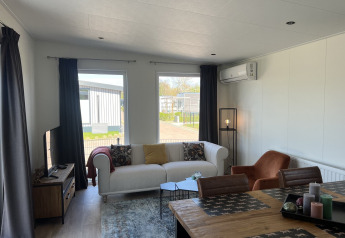 Salon d’un lodge Parkzicht au Vakantiepark de Zeeuwse Parel avec canapé, table à manger et grandes fenêtres.