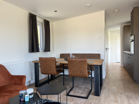 Comedor moderno en lodge con sillas marrones y mesa de madera en Parkzicht, Vakantiepark de Zeeuwse Parel.