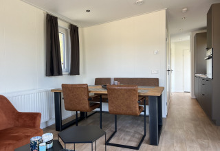 Moderne lodge spisestue med brune stole, træbord og lille køkken ved Parkzicht, Vakantiepark de Zeeuwse Parel.