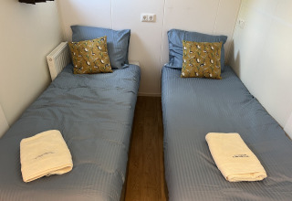 Two single beds with blue bedding, yellow accent pillows and towels at Parkzicht, Vakantiepark de Zeeuwse Parel.