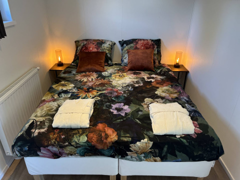 Cama doble con ropa de cama floral, dos cojines marrones y batas en Parkzicht, Vakantiepark de Zeeuwse Parel.