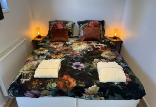 Doppelbett mit floralem Bettbezug, zwei braunen Kissen und Bademänteln im Parkzicht, Vakantiepark de Zeeuwse Parel.