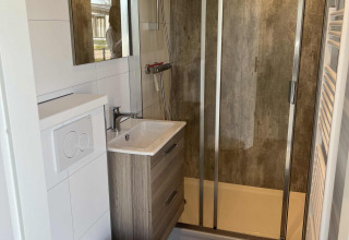 Moderne badeværelse med bruser, væghængt toilet og håndvask i en lodge på Parkzicht, Vakantiepark de Zeeuwse Parel.