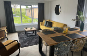 Salón comedor moderno de una cabaña en Vakantiepark de Zeeuwse Parel, Países Bajos, con sofá amarillo y grandes ventanales.