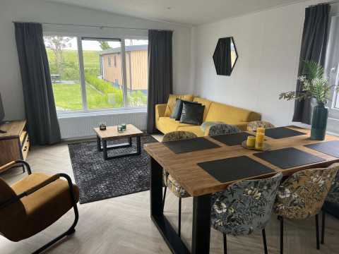 Salón comedor moderno de una cabaña en Vakantiepark de Zeeuwse Parel, Países Bajos, con sofá amarillo y grandes ventanales.