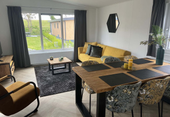 Salon moderne d'un lodge au Vakantiepark de Zeeuwse Parel, Pays-Bas, avec canapé jaune et grandes fenêtres.