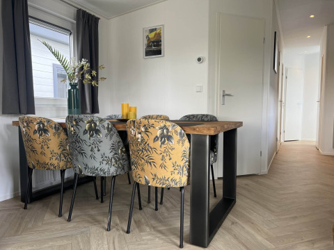 Comedor moderno de una cabaña en Vakantiepark de Zeeuwse Parel con sillas florales y mesa de madera.