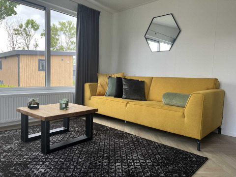 Intérieur moderne d'un lodge à Oosterschelde à Vakantiepark de Zeeuwse Parel avec canapé jaune et grande fenêtre.