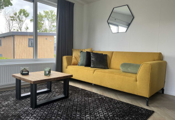 Modern lodge-interieur bij Oosterschelde in Vakantiepark de Zeeuwse Parel met gele bank en groot raam.