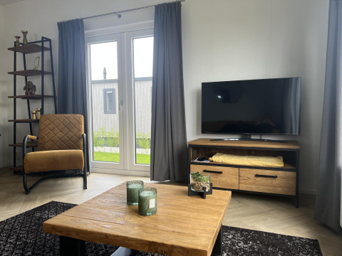 Salon moderne dans un lodge au Vakantiepark de Zeeuwse Parel avec télévision, fauteuil et table en bois.