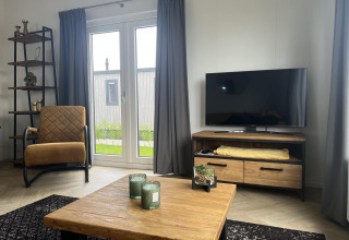 Sala moderna en una cabaña del Vakantiepark de Zeeuwse Parel, con televisor, sillón y mesa de madera.