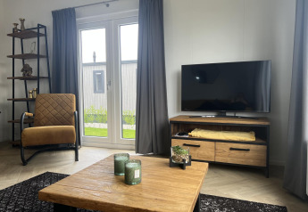 Salon moderne dans un lodge au Vakantiepark de Zeeuwse Parel avec télévision, fauteuil et table en bois.