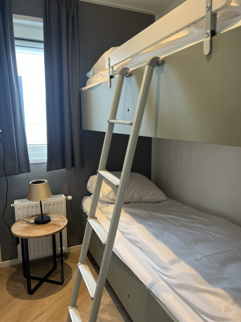 Habitación moderna con litera, escalera, mesa de madera y lámpara en la cabaña Oosterschelde, Países Bajos.