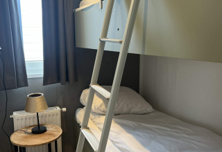 Habitación moderna con litera, escalera, mesa de madera y lámpara en la cabaña Oosterschelde, Países Bajos.