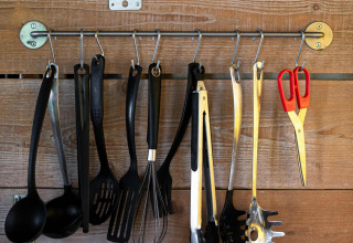 Utensilios de cocina cuelgan de ganchos en una pared de madera bajo una repisa en una Tentlodge safari.