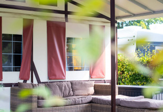 Udendørs siddeplads med rattan-sofa foran en safari-tentlodge med lyse gardiner og grønne planter.