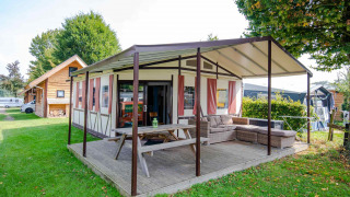 Tenda safari Tentlodge con veranda coperta, tavolo da picnic e divano su un campeggio erboso.