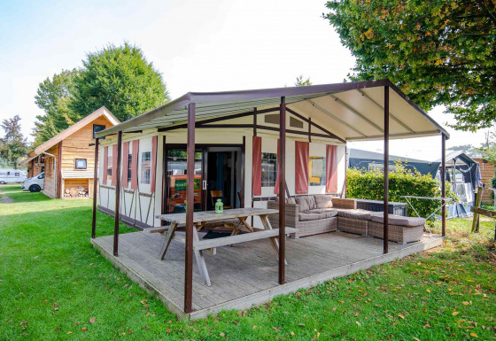 Tenda safari Tentlodge con veranda coperta, tavolo da picnic e divano su un campeggio erboso.