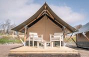 Tiny Tent Lodge auf Camping Waddenzee in den Niederlanden mit zwei Stühlen auf einer Holzterrasse.