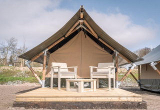Et billede af Tiny Tent-lodgen på Camping Waddenzee i Nederlandene, med to stole på en træterrasse.