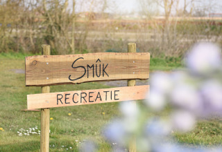 Træskilt med teksten 'Smûk Recreatie' i en feriepark i Friesland, Holland, på en grøn græsmark i foråret.