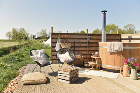 Espace extérieur avec terrasse en bois, bain nordique, fauteuils et fleurs chez Smûk Lytse Bell Tent, Pays-Bas.