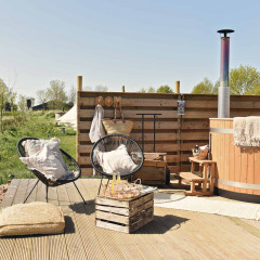 Espace extérieur avec terrasse en bois, bain nordique, fauteuils et fleurs chez Smûk Lytse Bell Tent, Pays-Bas.