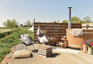 Buitenlounge met houten terras, hottub, stoelen en bloemen bij Smûk Lytse Bell Tent van Smûk Recreatie.