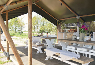 Buiteneetruimte onder een tent met houten tafels en banken bij Smûk Recreatie in Nederland.
