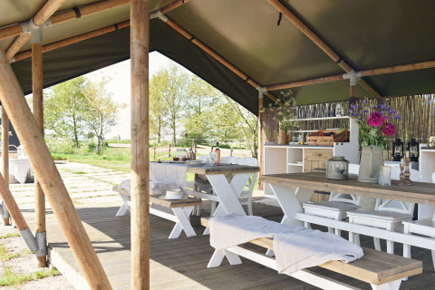 Zona de comedor al aire libre bajo una tienda tipi con mesas de madera en Smûk Recreatie, Países Bajos.