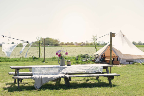 Ein Picknicktisch mit Blumen, weiße Zelt und Wäsche im Wind bei Smûk Recreatie, Niederlande, ländlich.