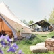 Smuk Lytse Bell Tent glamping-telt på grøn mark, med picnic-kurv og puder foran, og gamle bygninger bagved.