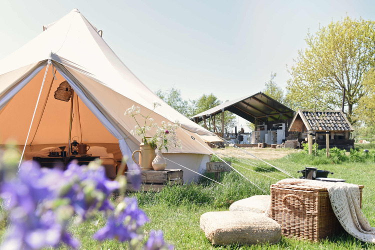 Escena de glamping en Smûk Lytse Bell Tent con tienda de campaña, cestas, cojines y ambiente rural.