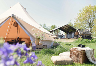 Smuk Lytse Bell Tent glamping-telt på grøn mark, med picnic-kurv og puder foran, og gamle bygninger bagved.