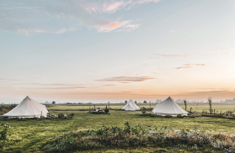 Sunrise over three teepee tents on a grassy field at Smûk Lytse Bell Tent, Smûk Recreatie, Netherlands.