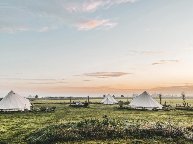 Zonsopgang boven drie tipi tenten op een grasveld bij Smûk Lytse Bell Tent, Smûk Recreatie, Nederland.