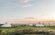 Sunrise over three teepee tents on a grassy field at Smûk Lytse Bell Tent, Smûk Recreatie, Netherlands.