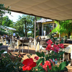 Terraza al aire libre en Camping Bella Italia en Véneto, Italia, con mesas, sillas, flores y vegetación.