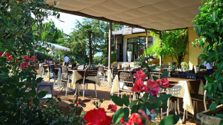 Terraza al aire libre en Camping Bella Italia en Véneto, Italia, con mesas, sillas, flores y vegetación.