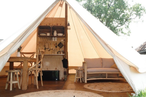 Binnenzicht van een safari tent met houten tafel, sofa en kitchenette bij Smûk Grutte Bell Tent.
