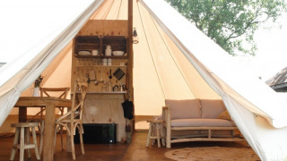 Interno di una tenda safari lussuosa con tavolo in legno, divano e cucinino da Smûk Grutte Bell Tent.