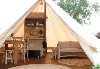 Interieur van een safari tent met houten meubels, een bank en een keuken bij Smûk Grutte Bell Tent.