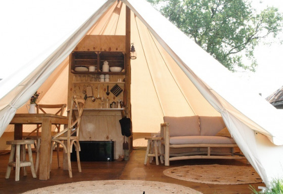 Indretning af en luksuriøs safari-telt med træmøbler, sofa og tekøkken hos Smûk Grutte Bell Tent.