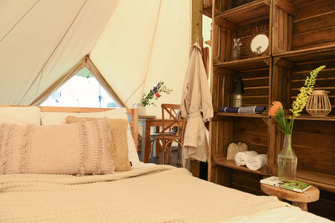 Gezellige binnenkant van de Smûk Grutte Bell Tent met bed, houten rekken en bloemen bij Smûk Recreatie.