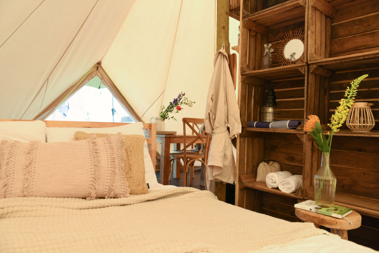 Innenansicht vom Safari-Zelt Smûk Grutte Bell Tent mit Bett, Holzregalen und Blumen bei Smûk Recreatie.