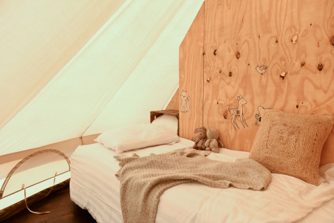 Gemütliches Bett in einem Smûk Grutte Bell Zelt, dekoriert mit Holzwand und Kuscheldecke.